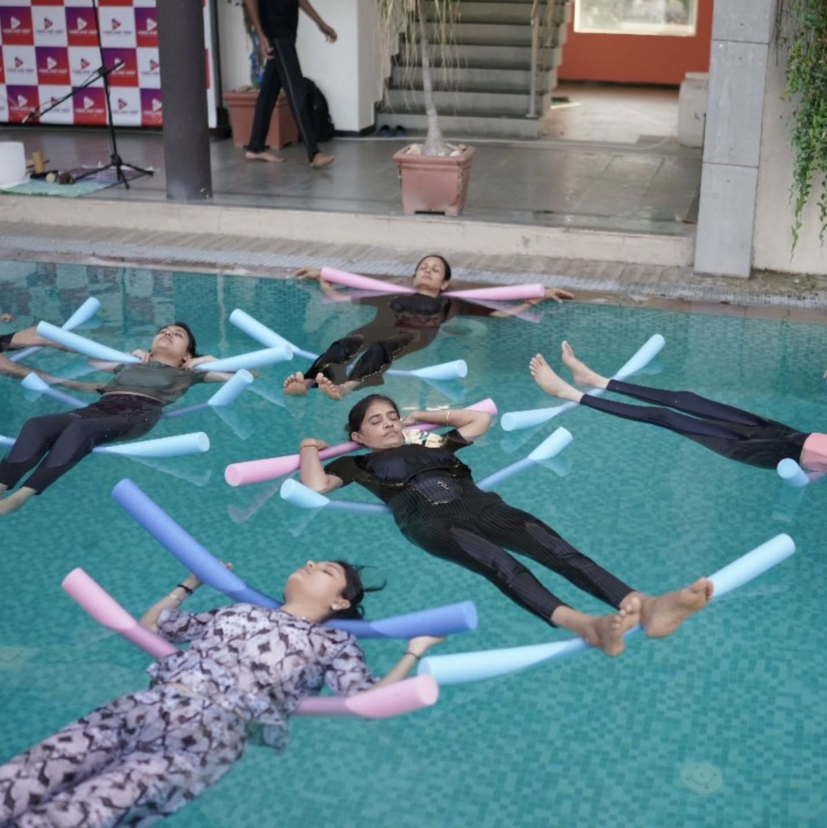 Group floating water therapy session with participants supported by pool noodles