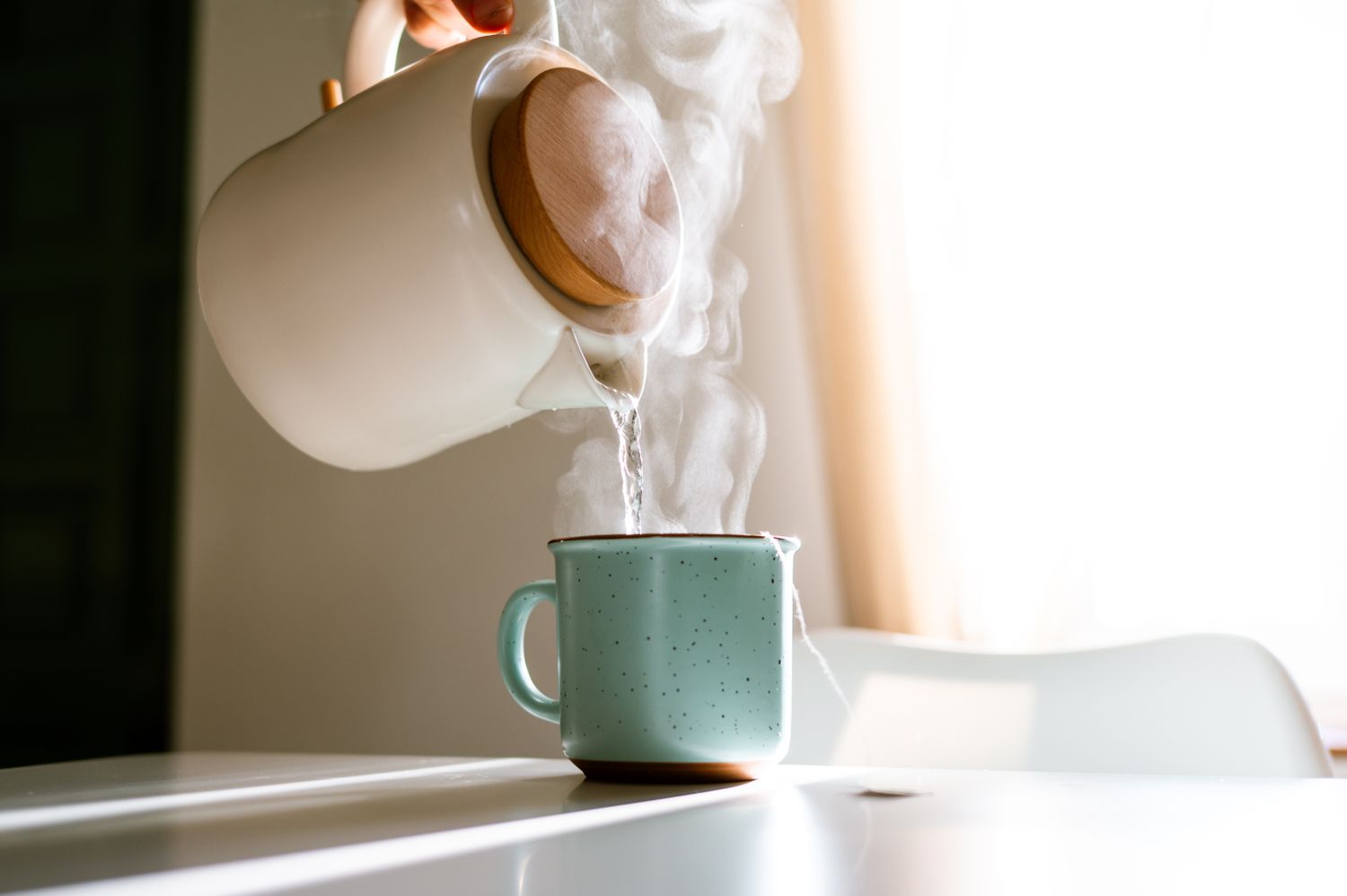 Steaming hot water being poured from a kettle into a mug